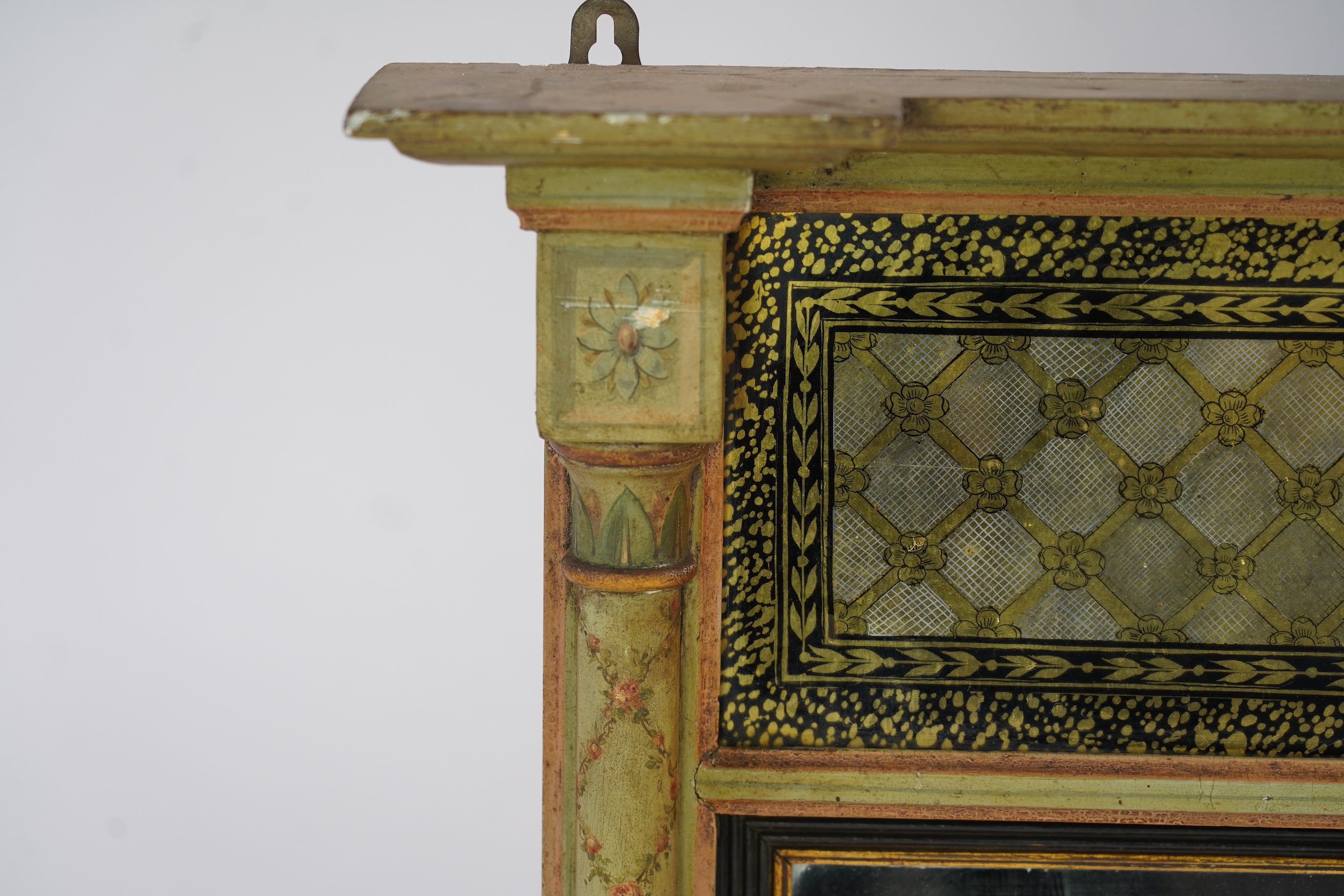 A Regency giltwood and composition overmantel mirror, with verre eglomise tablet frieze depicting a castle facade over a rectangular plate with reeded ebonised slip flanked by turned floral painted projecting columns, wi